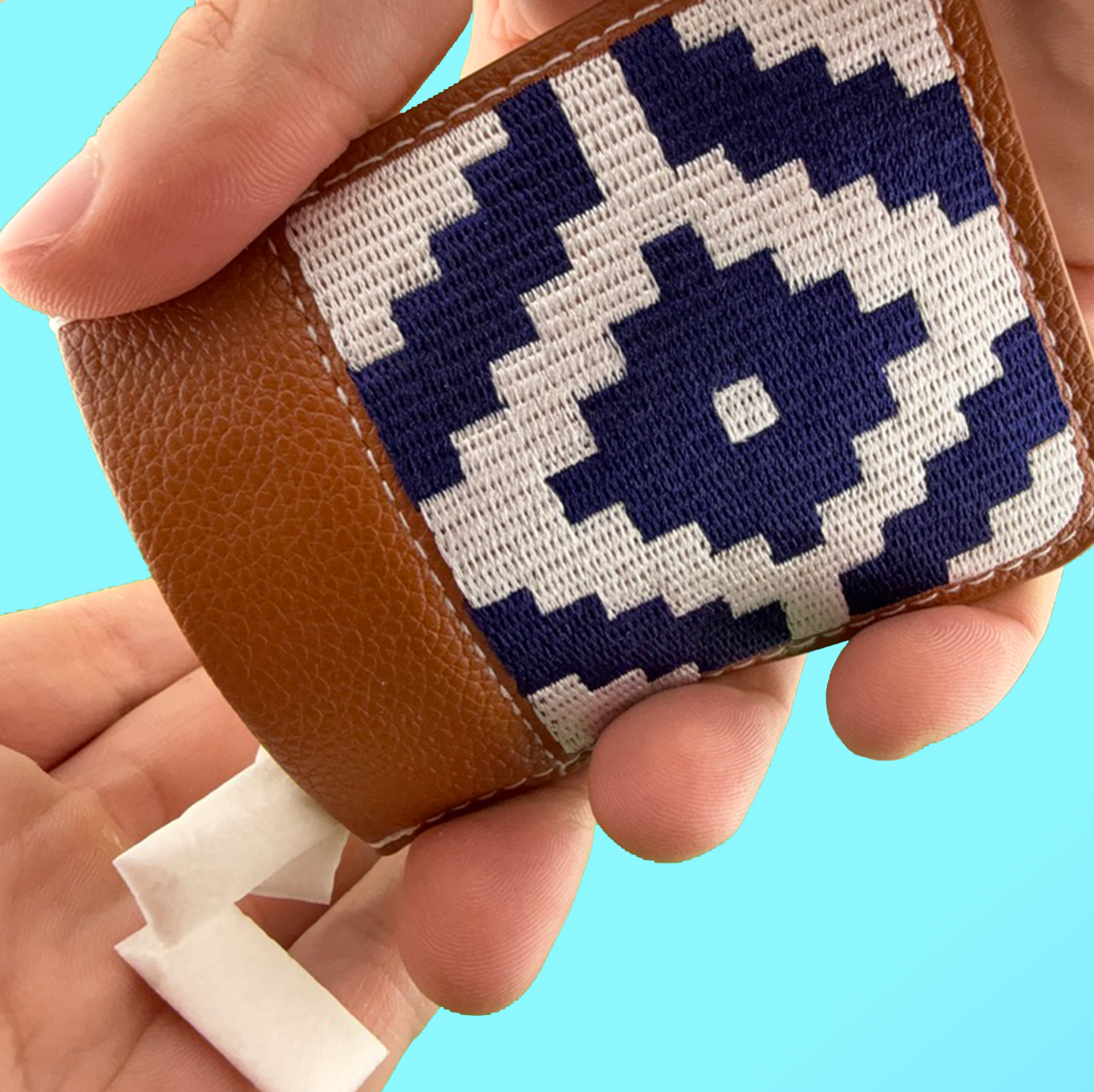 SLYD Hand holding a small woven pouch with a geometric pattern against a blue background
