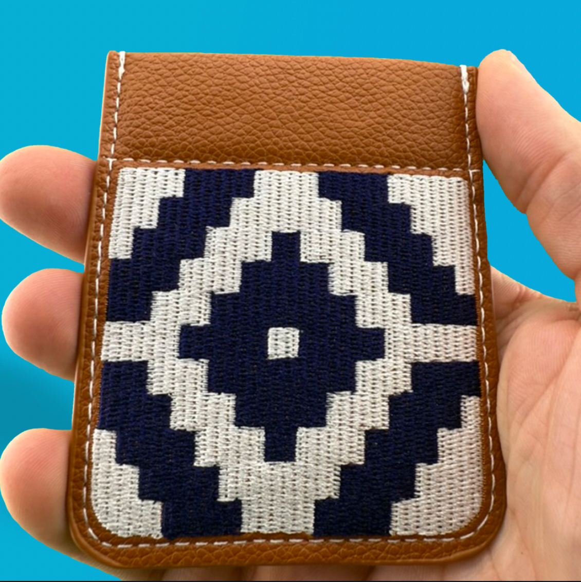 Small leather Madras Needlepoint SLYD with a pixelated eye design held in a hand against a blue background